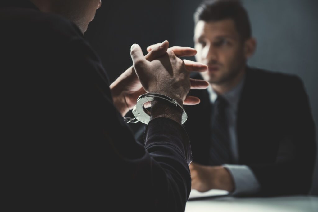 Criminal man with handcuffs being interviewed in interrogation room after committed a crime