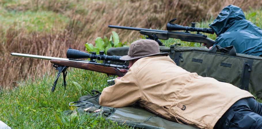 two men hunting with firearms while laying down