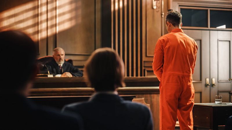 Man in orange jumpsuit standing before a judge on trial