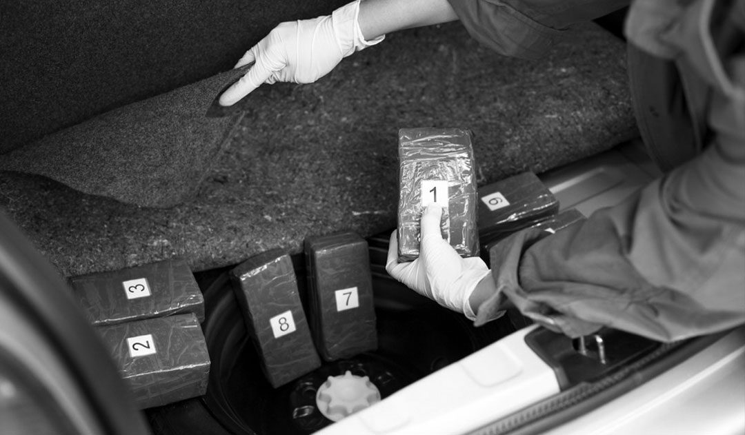 Drug Trafficking Arrest close up of police officer searching truck of car with multiple bags of drugs, drug trafficking arrest in michigan